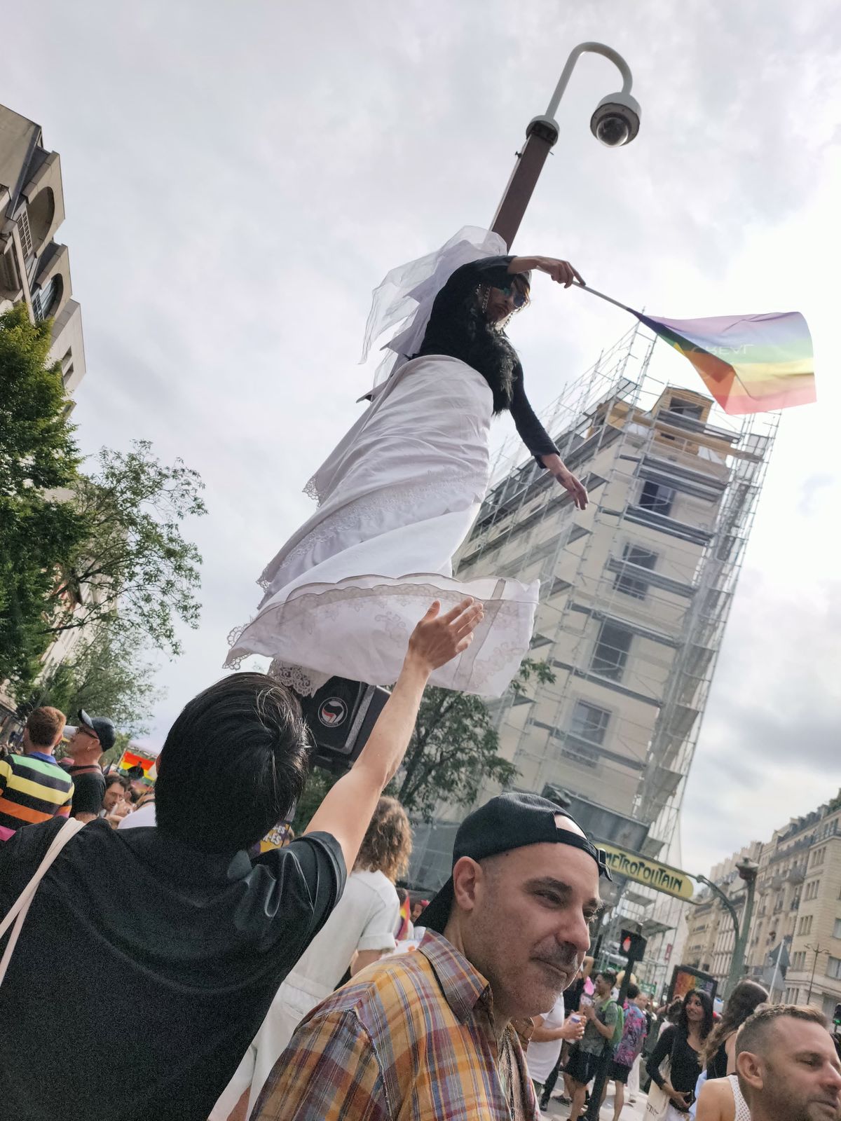 Ben en robe blanche au sommet d'un lampadaire, un drapeau à la main, la foule en dessous