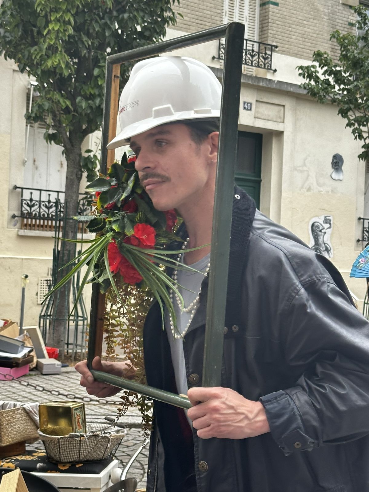 Ben de profil à travers un cadre vide, casque de chantier et bouquet de fleurs rouges